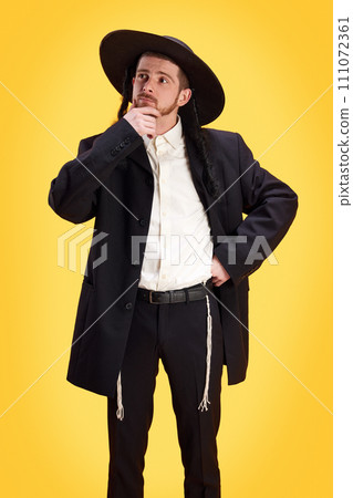 Portrait of Jewish man in traditional costume thinking about presents for his friends to Purim holiday against yellow background. Portrait of Jewish man in traditional costume thinking about presents for his friends to Purim holiday against yellow background. 111072361