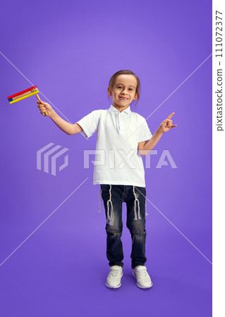 Little Jewish boy, kid playing with grogger against purple studio background. Celebration of Purim, national Jewish holiday. Little Jewish boy, kid playing with grogger against purple studio background. Celebration of Purim, national Jewish holiday. 111072377