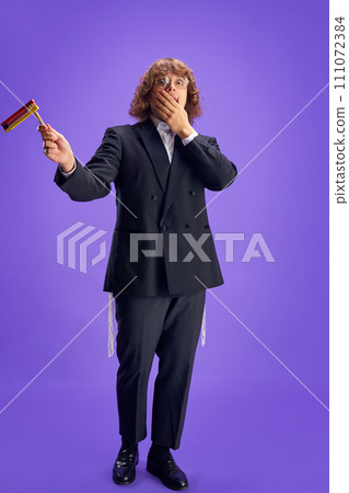 Full length portrait of young scared Jewish man holding grogger symbol used to drown out name of Haman villainous character. 111072384