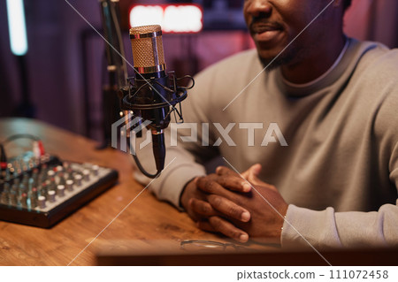 Cropped shot with focus on gold professional microphone on stand and Black man sitting at table recording live podcast 111072458