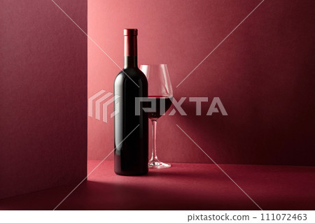 Bottle and glass of red wine on a red background. 111072463