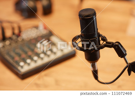 Close up shot of black condenser microphone in holder with defocused audio mixer board in studio room Close up shot of black condenser microphone in holder with defocused audio mixer board in studio room 111072469
