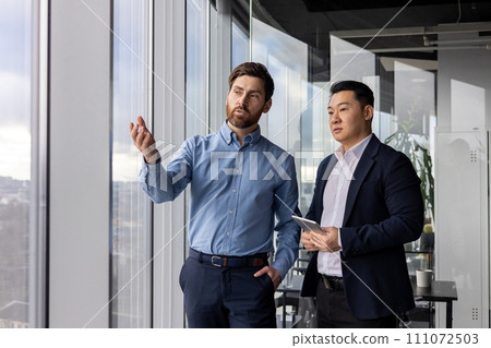 Two male corporate professionals engage in a serious discussion about business strategies in their well-lit office. Two male corporate professionals engage in a serious discussion about business strategies in their well-lit office. 111072503
