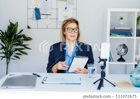 50's confident mature businesswoman, middle-aged experienced senior female professional recording video vlog webinar, online course. Female edtech entrepreneur shares skills, blogger online business. 111072675