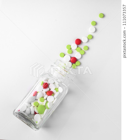 Pills spilling out from glass bottle on white background directly above Pills spilling out from glass bottle on white background directly above 111073357
