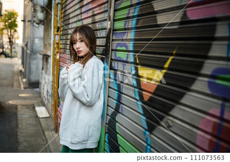 A young woman stands in front of a shutter with graffiti painted on it 111073563