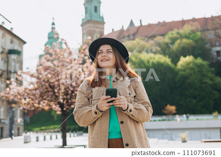 Modern Caucasian young woman 30s model with mobile phone looking at device on city street, wearing cute trendy outfit. Urban lifestyle concept. 30s female relaxing outdoors, spring time Modern Caucasian young woman 30s model with mobile phone looking at device on city street, wearing cute trendy outfit. Urban lifestyle concept. 30s female relaxing outdoors, spring time 111073691