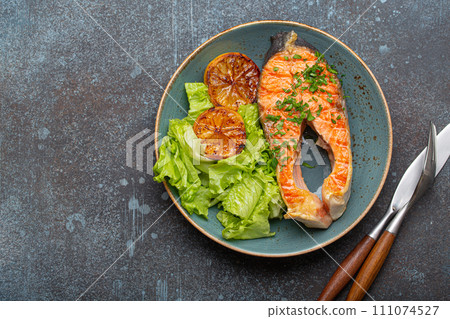 Grilled fish salmon steak and green salad with lemon on ceramic plate on rustic blue stone background top view, balanced diet or healthy nutrition meal with salmon and veggies, space for text Grilled fish salmon steak and green salad with lemon on ceramic plate on rustic blue stone background top view, balanced diet or healthy nutrition meal with salmon and veggies, space for text 111074527