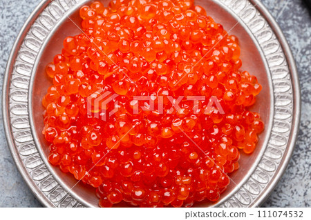 Small metal plate with red salmon caviar and a spoon top view on grey concrete background, festive luxury delicacy and appetizer Small metal plate with red salmon caviar and a spoon top view on grey concrete background, festive luxury delicacy and appetizer 111074532
