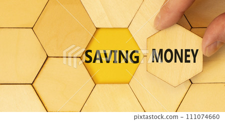 Saving money symbol. Concept words Saving money on beautiful wooden puzzles on a beautiful wooden background. Businessman hand. Business, support and saving money concept. Copy space. Saving money symbol. Concept words Saving money on beautiful wooden puzzles on a beautiful wooden background. Businessman hand. Business, support and saving money concept. Copy space. 111074660