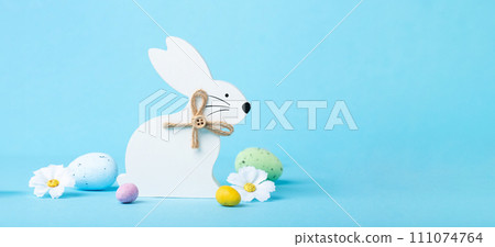 White Wooden Easter Bunny, Chocolate Eggs and Spring Flowers on Blue Background White Wooden Easter Bunny, Chocolate Eggs and Spring Flowers on Blue Background 111074764
