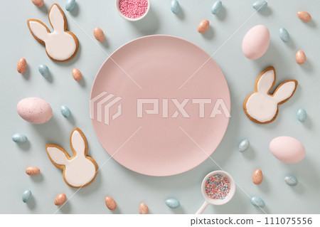 Easter homemade bunnies shaped cookies, eggs and pink plate as mock up on blue background. View from above. Festive food and snacks. Greeting card with space for text. 111075556