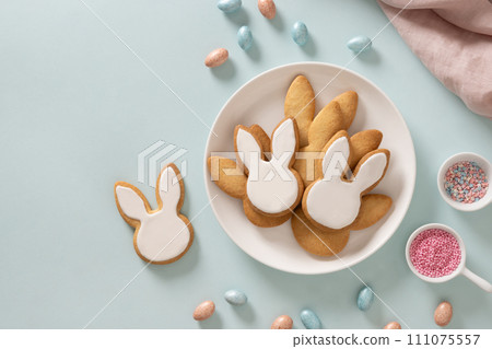 Easter homemade bunnies glazed shaped cookies and eggs on blue background. View from above. Festive food and snacks. Greeting card with space for text. 111075557