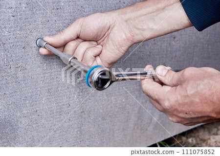 Finishing plinth on stilts with flat slate, worker uses socket wrench to tighten mounting screw. 111075852