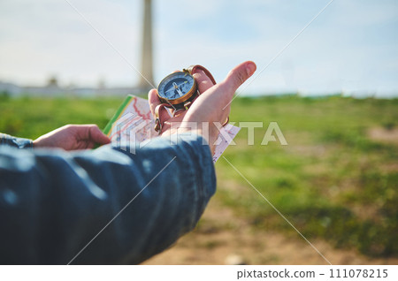 Close-up hands of a male hiker tourist traveler looking for directions with a compass, standing on the beach Close-up hands of a male hiker tourist traveler looking for directions with a compass, standing on the beach 111078215