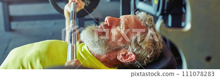 Pushing the limits of human body. Side view of a mature caucasian man lifting weighted bar or barbell at gym 111078283