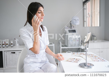 Female cosmetologist talking on smartphone at desk Female cosmetologist talking on smartphone at desk 111078823
