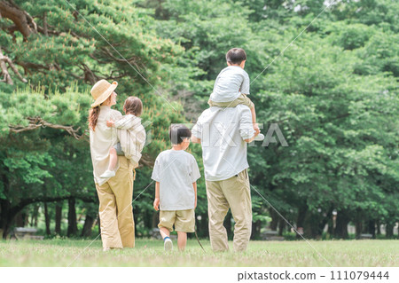 Rear view of a family walking hand in hand in the park during summer vacation (leisure, outdoors, picnic, camping) 111079444