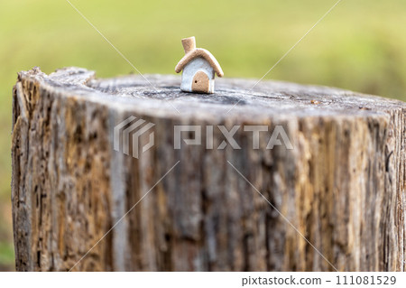 A small house with a cute rustic chimney made of unglazed earthenware placed on a log stump. A small house with a cute rustic chimney made of unglazed earthenware placed on a log stump. 111081529