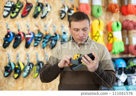 Man meticulously chooses climbing shoes in sports store 111081576