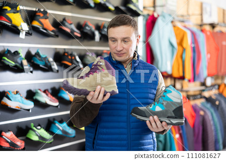 Attentive male athlete chooses sports winter shoes for hiking in sports store Attentive male athlete chooses sports winter shoes for hiking in sports store 111081627
