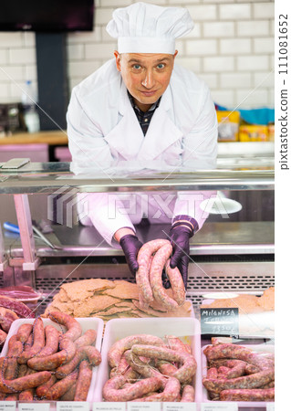 Butcher laying out raw sausages in showcase with price tags on Spanish 111081652