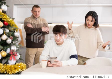 Quarrel during Christmas celebration - father and sister scolding young guy in home kitchen 111082107