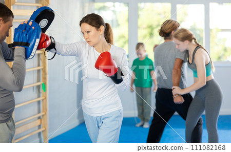 Woman works out strength and speed of boxing punch mitts with help of partner in boxing paws 111082168