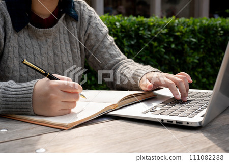 A cropped shot of a woman working on her business tasks at a table outdoors. 111082288