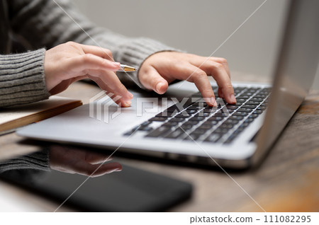 Close-up image of a woman typing on a keyboard, working on her laptop computer at a table. 111082295