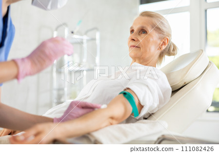 Senior woman getting collecting analysis in clinic. 111082426