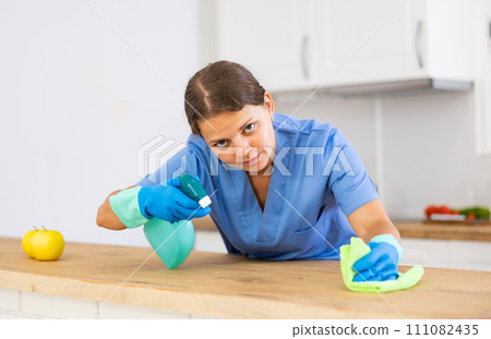 Woman in workwear cleaning countertop in kitchen 111082435