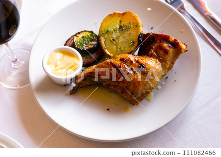 Fragrant fried rabbit leg with roasted potatoes on a ceramic plate served on a checkered tablecloth at home 111082466