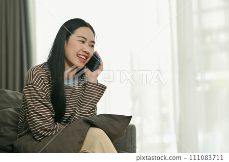 Attractive young woman having pleasant phone conversation while sitting on couch at home 111083711