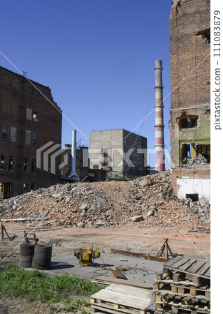 Abandoned factory with pipes, dilapidated brick buildings and pieces of walls under a clear blue sky 111083879
