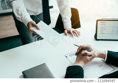 Male employee handed out a resignation envelope to the manager. Male employee handed out a resignation envelope to the manager. 111084597