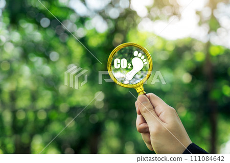 Businessman's hand holding a magnifying glass with carbon footprint eco friendly concept. 111084642