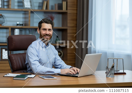 Smiling caucasian man in wired headphones looking at camera and holding hands on laptop keyboard. Optimistic entrepreneur listening to music while making routine task for getting rid of boredom. Smiling caucasian man in wired headphones looking at camera and holding hands on laptop keyboard. Optimistic entrepreneur listening to music while making routine task for getting rid of boredom. 111087515