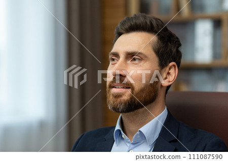 Confident caucasian man with trendy hairstyle looking ahead inspired on blurred background. Satisfied male boss listening to quarterly report with impressive results from hired employee in cabinet. Confident caucasian man with trendy hairstyle looking ahead inspired on blurred background. Satisfied male boss listening to quarterly report with impressive results from hired employee in cabinet. 111087590
