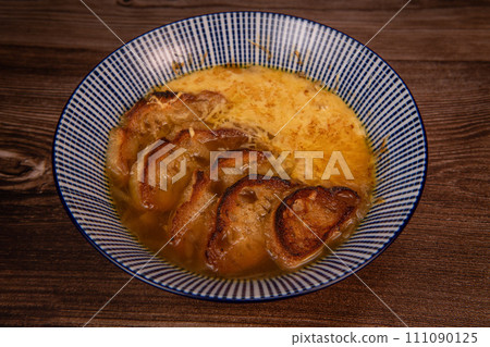 Classic French onion soup baked with cheese croutons sprinkled with fresh thyme, close up view. 111090125
