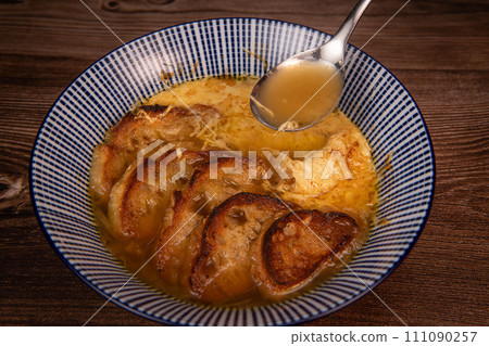 Classic French onion soup baked with cheese croutons sprinkled with fresh thyme, close up view. 111090257