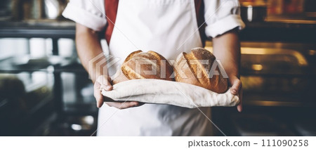 Baker Holding Two Freshly Baked Loaves of Bread 111090258