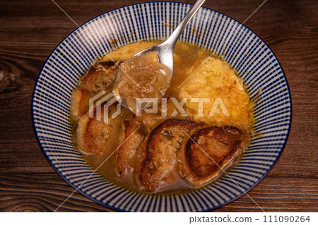Classic French onion soup baked with cheese croutons sprinkled with fresh thyme, close up view. 111090264