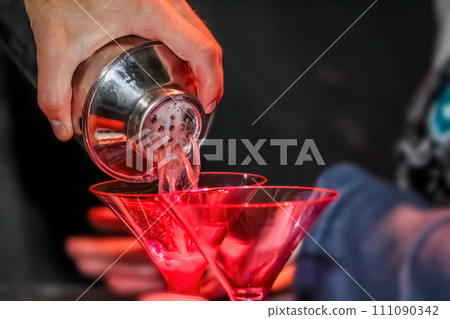 A close up to bartender expertly pouring a mixed drink, gracefully pouring it into a martini glass. A close up to bartender expertly pouring a mixed drink, gracefully pouring it into a martini glass. 111090342