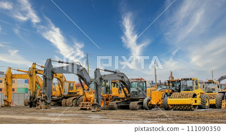 Various heavy construction vehicles, such as excavators, diggers, earthmovers, and bulldozers, are stationed at a construction site throughout the winter season. 111090350