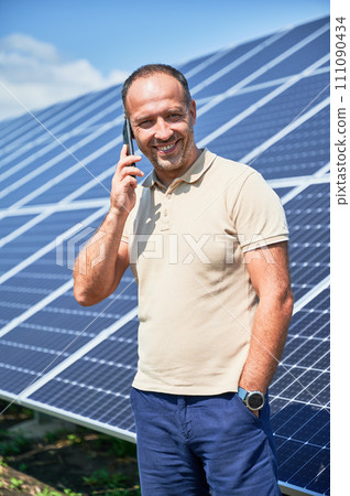 Happy businessman having important call. Man talking about his investment in alternative energy resource. Man taking on phone on background of solar panels. 111090434