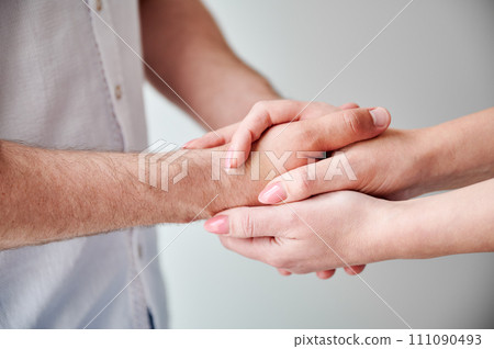 Close up of two hands engaging in delicate touch. Man's and woman's hands on white neutral background. Husband holding hand of his lovely wife. Concept of affection, support, and mutual respect. 111090493