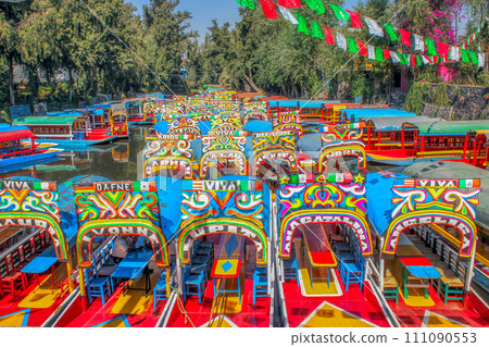 Mexico City, Mexico. Jan 15, 2024. An horizontal view of Several Trajineras or gondolas style boats, or colourful rafts parked along the Xochimilco canal. Mexico City, Mexico. Jan 15, 2024. An horizontal view of Several Trajineras or gondolas style boats, or colourful rafts parked along the Xochimilco canal. 111090553