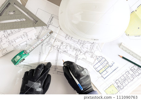 Top view of a contractor hands with pencil working on Architecture plans on desk of a construction site 111090763