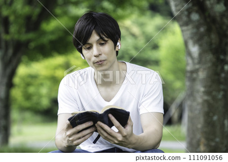 A foreign man reading while listening to music in a fresh green park A foreign man reading while listening to music in a fresh green park 111091056